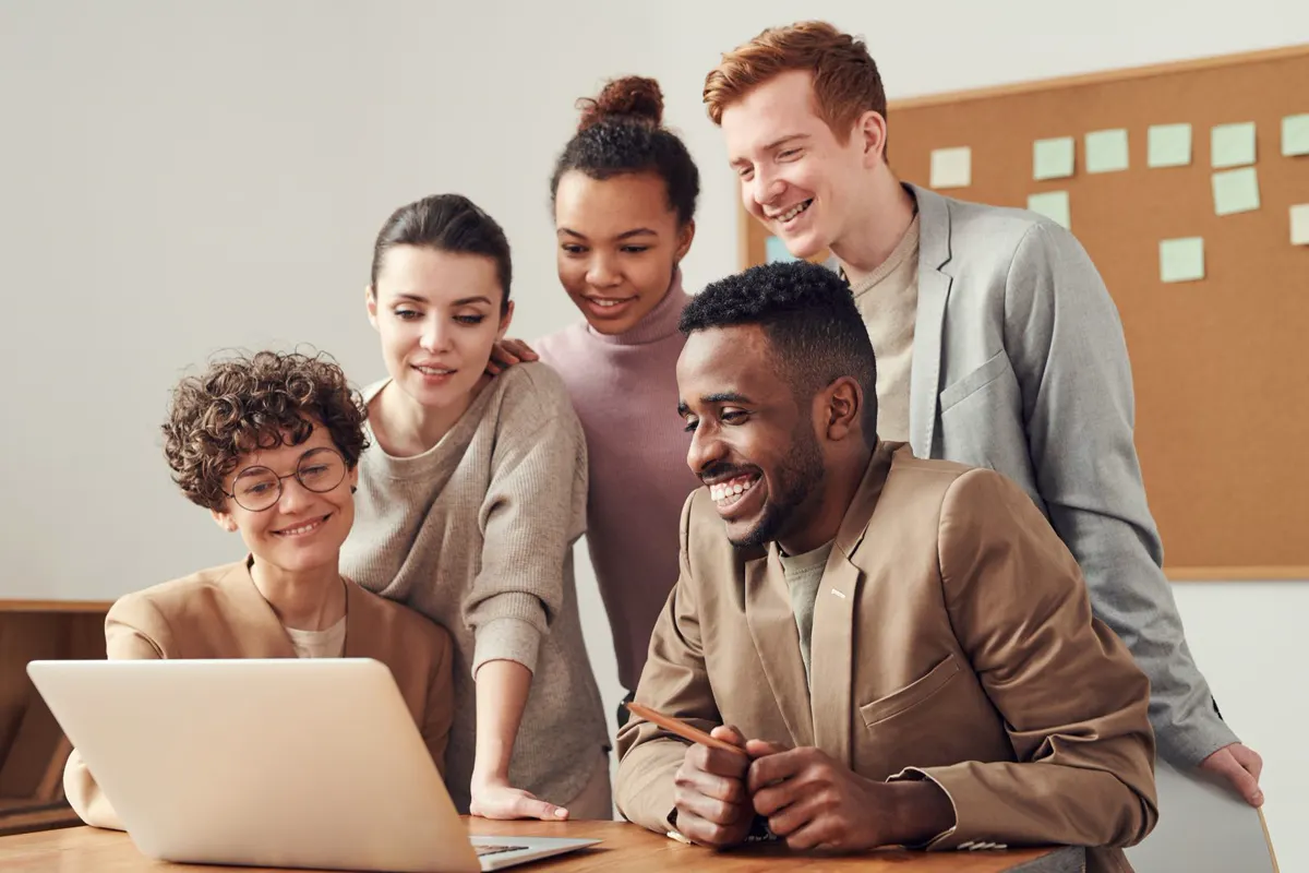Illustrative stock photo, not a client: five colleagues gathered around a laptop in a bright office, reviewing something together.